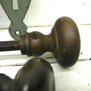 May include: A pair of vintage brass door knobs with a rounded, smooth finish and a dark, aged patina. Each knob features a central metal spindle extending from the base, with a small visible screw securing the neck of the hardware component.