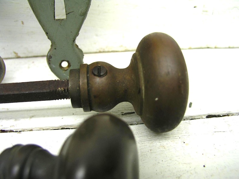 May include: A pair of vintage brass door knobs with a rounded, smooth finish and a dark, aged patina. Each knob features a central metal spindle extending from the base, with a small visible screw securing the neck of the hardware component.