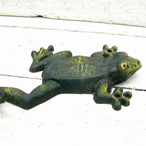 May include: A green cast iron frog figurine with yellow accents. The frog is posed with its legs outstretched and its head turned to the side.