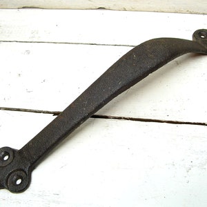 May include: A black cast iron door handle with a decorative design. The handle is curved and has a smooth finish.