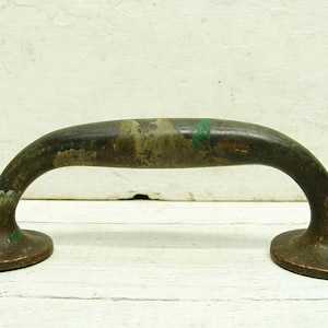 May include: Antique brass door pull handle with a rounded shape and two circular bases. The handle has a worn, aged patina with green accents.