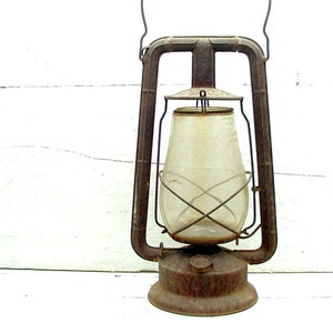 May include: Vintage metal lantern with a clear glass globe and a rusty brown finish. The lantern has a handle for carrying and a base for stability. The glass globe has a cross-wire design.