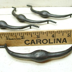 May include: Four antique metal drawer pulls with a rounded, teardrop-shaped design. The pulls are approximately 3 inches long and are shown next to a ruler.