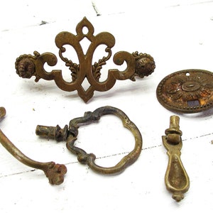 May include: An assortment of antique brass hardware, including drawer pulls and decorative backplates. The pieces feature ornate designs with floral and scrollwork details. The hardware has a weathered, aged appearance, suggesting vintage or salvaged origins.
