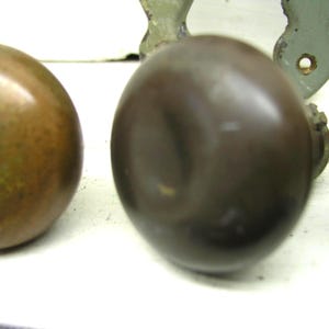 May include: A set of round, dark brown metal door knobs with a smooth, reflective surface. The knobs are positioned in a row, showing a spherical shape and a metallic finish. Each knob is attached to a base component, displaying a consistent design.