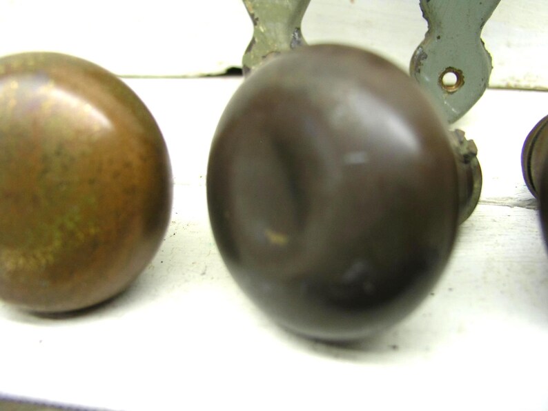 May include: A set of round, dark brown metal door knobs with a smooth, reflective surface. The knobs are positioned in a row, showing a spherical shape and a metallic finish. Each knob is attached to a base component, displaying a consistent design.