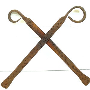 May include: A pair of rusty metal fireplace tools with looped handles, crossed and resting on a white surface.
