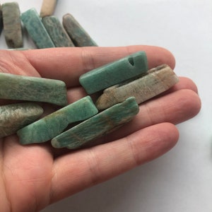 May include: A collection of green and white amazonite gemstone beads, each with a hole drilled through the centre. The beads are smooth and polished, with a natural, organic shape.