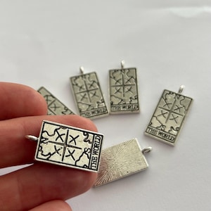 May include: Five silver charms featuring the tarot card "The World". Each charm has a black and white image of the card's symbol and the text "The World".