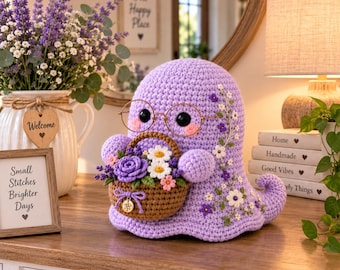 May include: A lavender crochet ghost figure wearing gold-rimmed glasses and holding a brown woven basket filled with crocheted flowers. The ghost features embroidered floral details on its side and a small charm attached to the basket handle.
