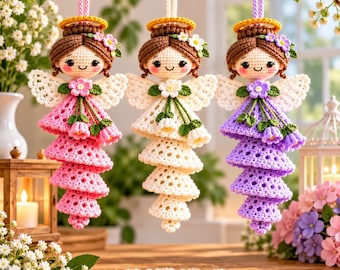 May include: Three crocheted angel ornaments hanging from a branch. Each angel features brown yarn hair, a yellow halo, white lace wings, and a tiered dress in pink, white, or purple, accented with small crocheted flowers and green leaves.