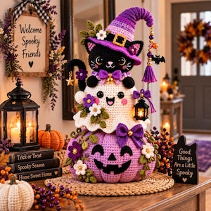 May include: A crochet Halloween display featuring a purple-hatted black cat sitting atop a white ghost, which rests on a large purple jack-o'-lantern. The figures are decorated with small flowers, bows, and a miniature lantern, all crafted in yarn.