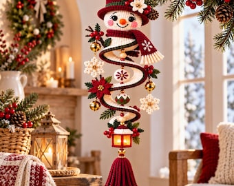 May include: A crocheted snowman ornament featuring a red top hat, a matching scarf, and a spiral body. The decoration is adorned with white snowflakes, red poinsettias, gold bells, and a small lantern at the base, finished with a red tassel.
