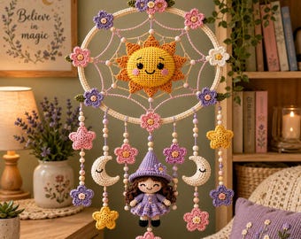 May include: A crochet wall hanging featuring a central yellow sun with a smiling face, surrounded by a circular frame decorated with pink, purple, and white flowers. Below, a small crochet doll in a purple hat hangs with stars and moons.