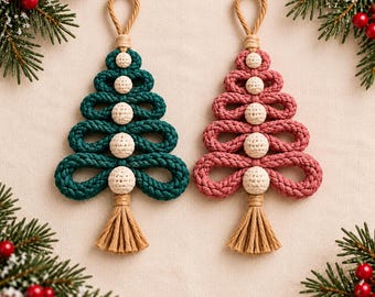 May include: Two macrame Christmas tree ornaments, one in dark green and one in dusty rose, each featuring a looped rope design, cream-colored crocheted beads, a top hanging loop, and a tan tassel at the base, accented by pine branches.