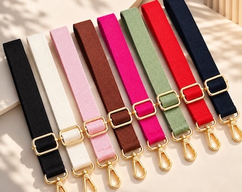 May include: A set of eight adjustable bag straps in black, white, light pink, brown, hot pink, sage green, red, and navy blue. Each strap features gold-toned metal hardware, including a sliding buckle for length adjustment and a swivel lobster clasp.