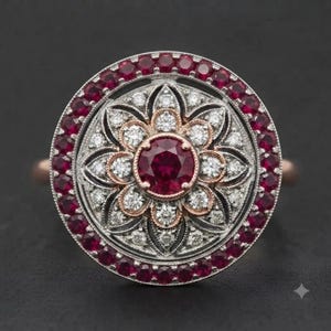 May include: A circular ring featuring a central round-cut red ruby surrounded by a floral pattern of small white diamonds set in silver metal. The center is framed by a rose gold border, with an outer halo of round red rubies set in silver.