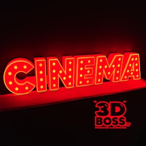 Può includere: Un'insegna luminosa rossa che forma la parola CINEMA in lettere stampatello, caratterizzata da una griglia di piccole luci circolari sulla faccia di ogni carattere. L'insegna brilla su sfondo scuro, con un logo 3D BOSS.IT nell'angolo.