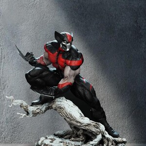May include: A detailed figurine of a muscular character in a black and red suit with a silver mask, crouching on a textured, weathered tree branch. The character has sharp claws extended from each hand. The logo goldenfast is visible in the top right.