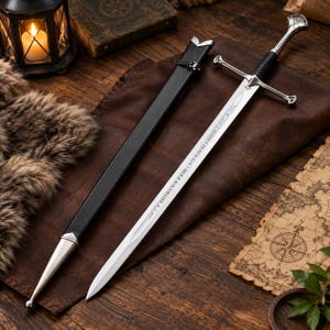 May include: A silver-toned metal sword with a black wrapped grip, a cross-shaped guard, and a pointed blade featuring etched runic inscriptions. The sword is accompanied by a black scabbard with silver-toned metal fittings at the tip and top.