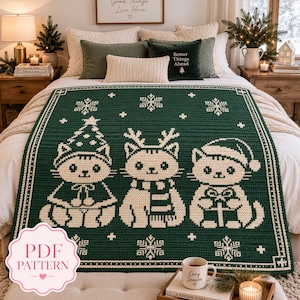 Peut inclure: Une couverture en crochet vert foncé avec un motif blanc représentant trois chats portant des accessoires de fête, dont un chapeau sapin, des bois de renne et un bonnet de Noël, entourés de petits flocons de neige blancs.