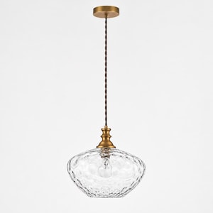 May include: A pendant light fixture featuring a clear, dimpled glass shade with a rounded, flattened shape. The light is suspended by a twisted brown cord from a circular brass ceiling canopy, with a brass-toned metal socket holder.