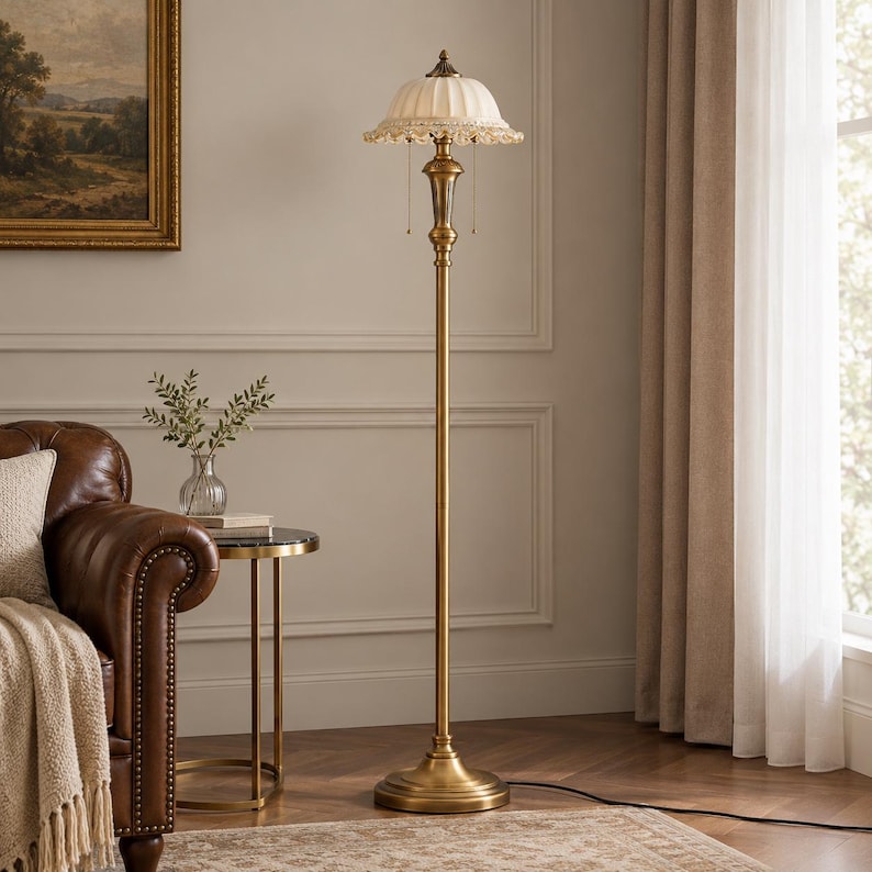 Puede incluir: Una l&aacute;mpara de pie con un soporte de metal de tono lat&oacute;n alto y delgado y una base circular. La l&aacute;mpara cuenta con una pantalla blanca plisada en forma de c&uacute;pula con un borde decorativo de flecos de cuentas y dos interruptores de cadena.