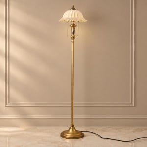 May include: A floor lamp with a tall, slender brass-toned metal stand and a circular base. The lamp features a cream-colored, pleated fabric shade with a scalloped edge and dangling clear crystal accents, topped with a small brass finial.