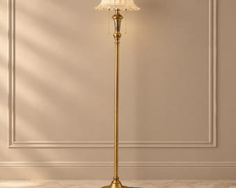 May include: A floor lamp with a tall, slender brass-toned metal stand and a circular base. The lamp features a cream-colored, pleated fabric shade with a scalloped edge and dangling clear crystal accents, topped with a small brass finial.