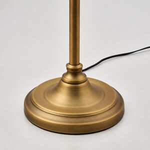 Puede incluir: Una base de l&aacute;mpara de metal en tono lat&oacute;n con un pedestal circular escalonado y un v&aacute;stago vertical delgado. Un cable el&eacute;ctrico negro fino se extiende desde la base hacia un lado. El acabado tiene una apariencia met&aacute;lica cepillada.