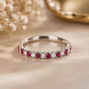 May include: A silver-toned eternity band featuring an alternating pattern of round-cut red rubies and clear white diamonds set in a shared-prong metal setting. The ring displays a continuous row of gemstones encircling the entire band.