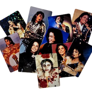 May include: A collection of rectangular trading cards featuring various photographic portraits of Michael Jackson in different outfits and poses, including one card where he is dressed as a clown with white face paint and a ruffled collar.