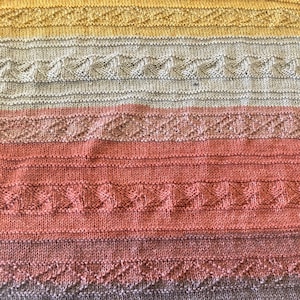 May include: A knitted throw blanket with a striped pattern in shades of yellow, gray, pink, and brown.