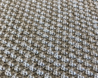 May include: Close-up of a knitted fabric with a textured pattern. The fabric is a mix of brown and gray yarn.