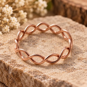 May include: A rose gold ring featuring a continuous twisted wire design. The band is formed by two thin metal strands intertwined in a repeating pattern, creating a circular shape with a smooth, polished metallic finish throughout the entire piece.