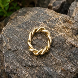 May include: A polished gold-tone ring featuring a continuous twisted rope design. The band is formed by two strands of metal intertwined to create a circular shape with a smooth, reflective surface and a uniform thickness throughout the entire piece.