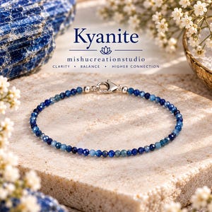 Könnte beinhalten: Ein zartes Armband aus kleinen, facettierten blauen Kyanitperlen mit einem silberfarbenen Karabinerverschluss. Der Text Kyanite, mishucreationstudio und die Wörter CLARITY, BALANCE, HIGHER CONNECTION sind über dem Schmuckstück zu sehen.