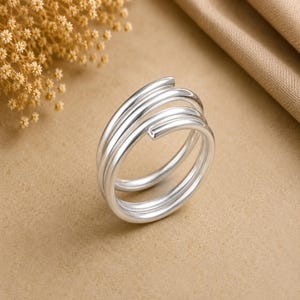 May include: A silver-toned ring featuring a multi-layered spiral design. The band consists of three continuous, smooth, polished loops that wrap around to form a single cohesive piece of jewelry with a reflective, metallic finish.
