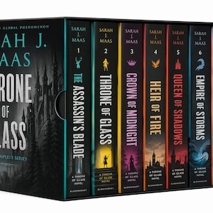Op de afbeelding: Een boxset van acht Throne of Glass-romans van Sarah J. Maas. De zwarte doos bevat een illustratie van een bos en kasteel. Elke boekrug toont een unieke kleur, titel en icoon, waaronder The Assassin's Blade, Throne of Glass, Crown of Midnight, Heir of Fire, Queen of Shadows, Empire of Storms, Tower of Dawn en Kingdom of Ash.