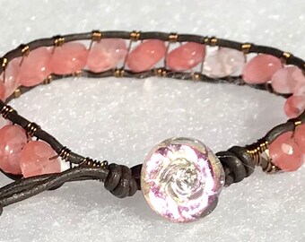 May include: A brown leather bracelet with pink and clear gemstone beads and a rose-shaped glass bead.
