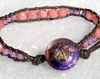 May include: A brown leather bracelet with pink and purple beads and a dragonfly button closure.
