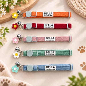 May include: Five fabric cat collars in orange, red, pink, green, and blue. Each collar features a silver bell, a flower charm, a cat-shaped buckle, and a white rectangular tag printed with the name BELLA and the phone number 123-456-7890.
