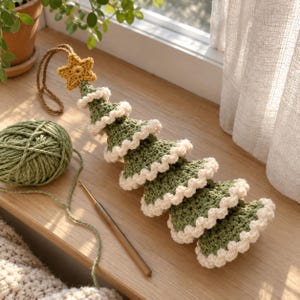 May include: A handmade crochet Christmas tree ornament in olive green with cream-colored ruffled edges. The tree is topped with a small mustard yellow crocheted star and features a brown yarn loop for hanging, accompanied by a ball of green yarn.