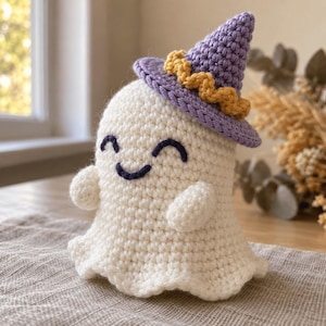 May include: A white crocheted ghost figurine featuring a smiling face with dark blue stitched eyes and a mouth. The ghost wears a pointed purple crocheted witch hat adorned with a textured yellow band around the base, crafted from yarn.