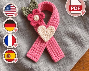 May include: A pink crochet awareness ribbon featuring a small pink flower with a cream center, two olive green leaves, and a cream-colored heart attached to the front. A circular icon with the text PDF is visible in the upper right corner.
