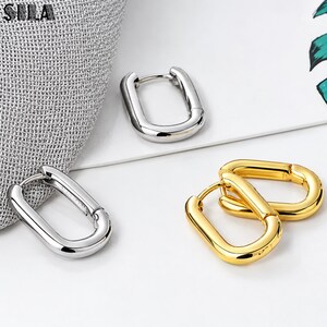 May include: Three oval-shaped hoop earrings with a smooth, polished finish. One earring is silver-toned, while the other two are gold-toned. Each earring features a hinged post mechanism for closure, showcasing a simple, rounded, and continuous metal loop design.