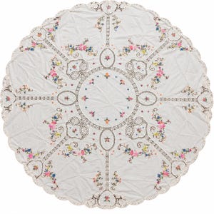 Könnte beinhalten: Eine runde weiße Tischdecke mit aufwendigen Lochstickerei-Rändern und bunter Blumenstickerei. Das Design umfasst ein zentrales kreisförmiges Motiv, umgeben von symmetrischen Blumenranken in Rosa, Blau und Gelb, mit einem gewellten Rand.