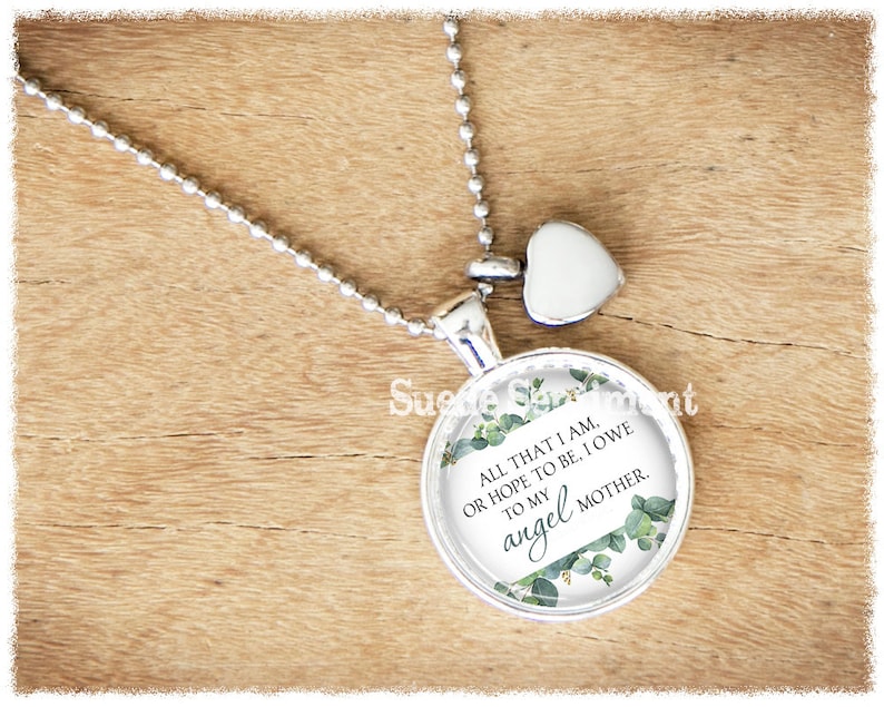 May include: Silver necklace with a round pendant featuring a floral design and the text "ALL THAT I AM. OR HOPE TO BE, I OWE TO MY angel MOTHER."