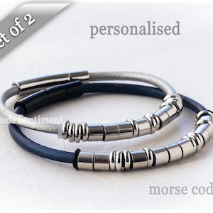 May include: Set of two personalized leather bracelets with silver metal beads. The bracelets are in blue and white leather. The text "morse code" is visible below the bracelets.