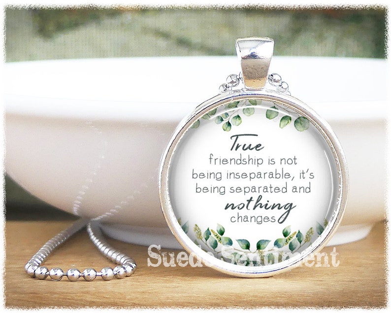 May include: Silver necklace with a round glass pendant featuring a green leafy design and the quote "True friendship is not being inseparable, it's being separated and nothing changes".